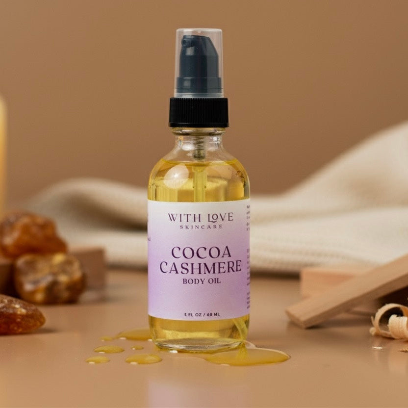 Bottle of Cocoa Cashmere body oil with a label on a wooden surface with candles and stones.