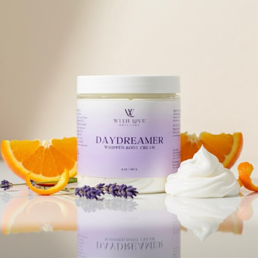Jar of 'Daydreamer' whipped body cream with orange slices and lavender on a reflective surface.